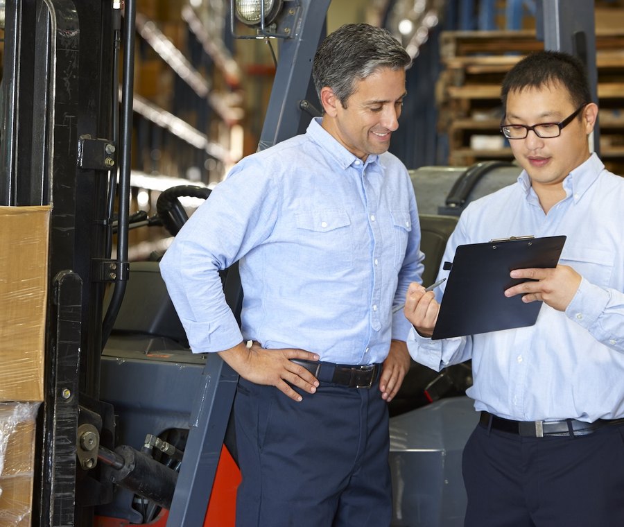 Two managers reviewing operations on a tablet beside a forklift