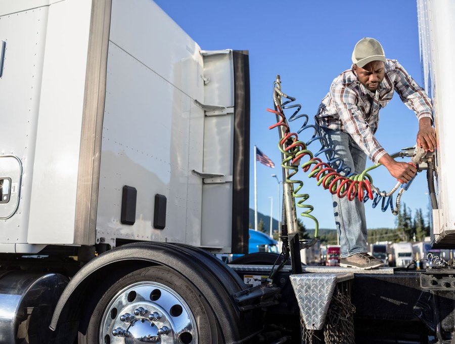 Driver connecting brake and air lines to a trailer at a freight yard